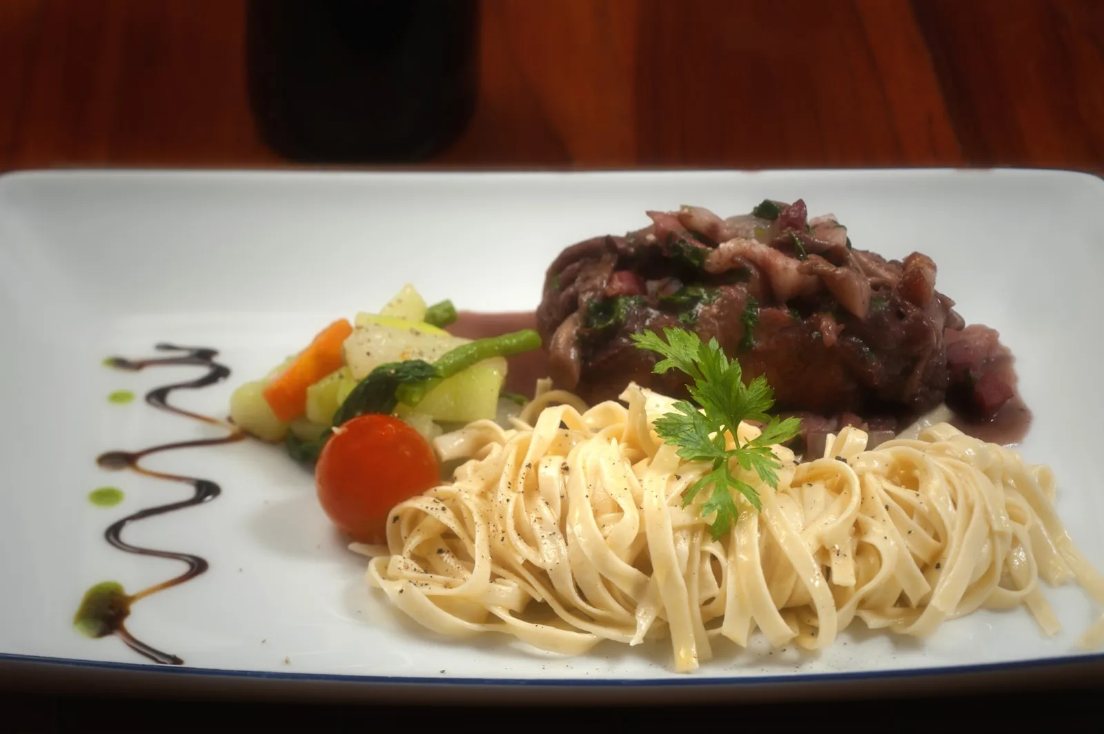 Coq au vin servi avec des tagliatelles et des légumes.